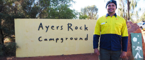 Indigenous job seeker in front of Ayers Rock Campground sign